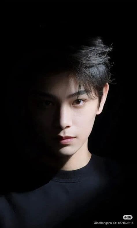 Intense masculine portrait in a dark studio setting with soft directional key light carving out strong facial bone structure.