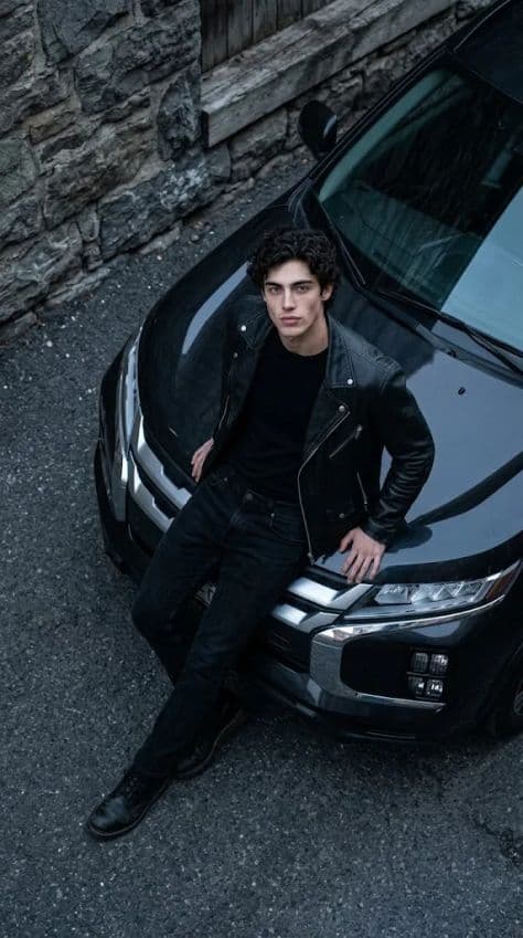 High-angle overhead portrait of a man leaning on the hood of a charcoal black Mitsubishi SUV