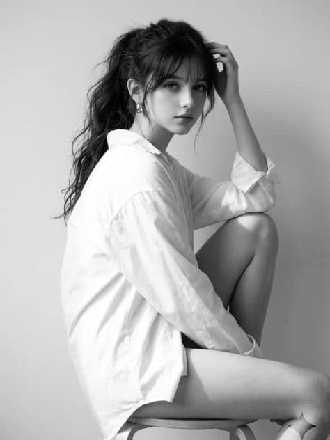 Black and white studio portrait of a woman seated sideways on a stool looking back at the camera