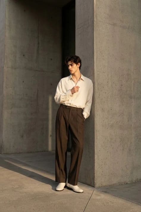 Editorial fashion portrait of a man in an oversized ivory shirt beside a monumental concrete building