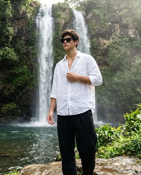 An adventurer standing on a wet granite ledge beside a clear mountain pool fed by twin waterfalls.