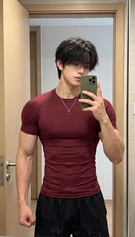 Athletic man taking an indoor mirror selfie with phone wearing a deep burgundy athletic compression shirt.