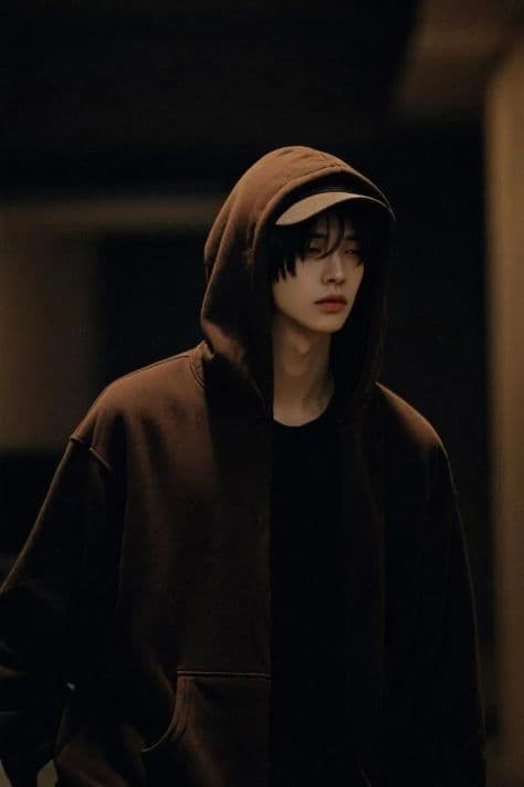Young man in a rich espresso-brown hoodie standing in a dim courtyard illuminated by soft lantern glow.