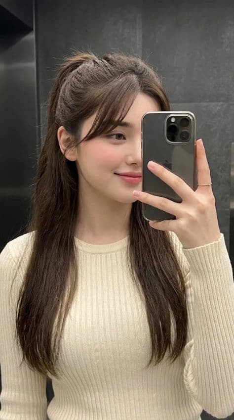 Girl taking a 3/4 mirror selfie in a cream ribbed knit top and half-up ponytail