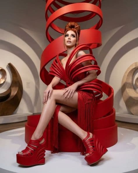 Red-haired woman in sculptural couture gown standing in a grand hall with dramatic light