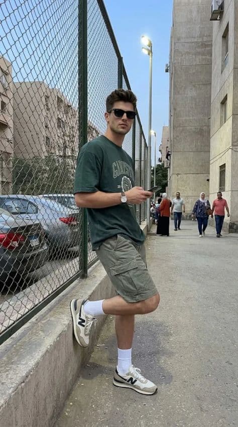 Young man in oversized green tee and shorts standing at a Cairo basketball court at dusk