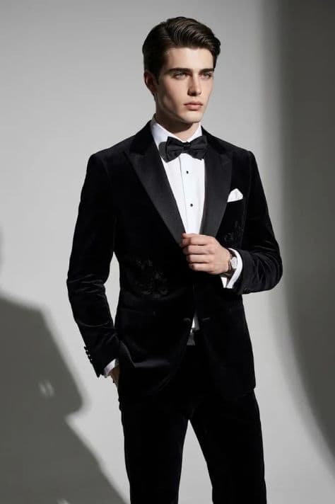 Man in a black velvet tuxedo with satin peak lapels and black bow tie in photo studio