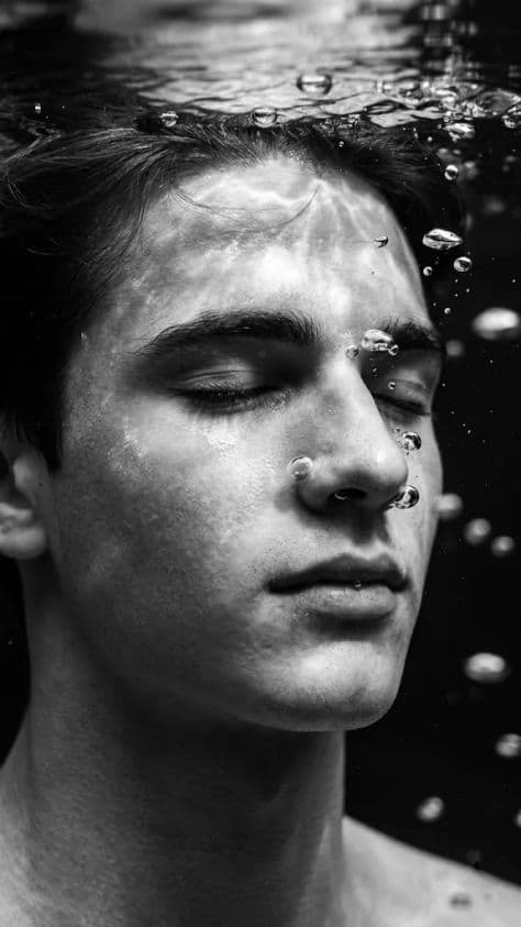 Peaceful underwater close-up of a person floating with closed eyes and rising air bubbles in clear blue water