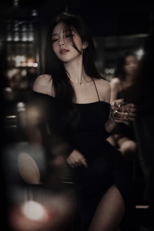 Cinematic low-light portrait of a Korean idol-inspired woman in a dim lounge bar setting with warm tungsten lighting, shallow depth of field, and moody editorial fashion photography style.