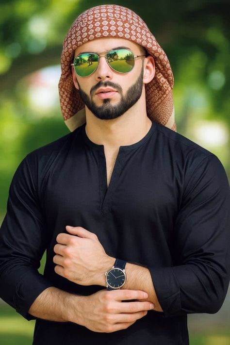 Photorealistic vertical outdoor portrait of a young man wearing a pure black kurta, burnt red patterned keffiyeh, gold aviator sunglasses with green mirrored lenses, and a visible wristwatch while posing in a warm blurred garden background.