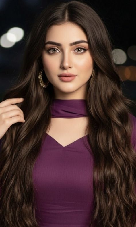 Photorealistic vertical nighttime portrait of a young woman wearing a fitted deep plum-purple outfit with a matching neck scarf, long dark chocolate-brown wavy hair, partially hidden gold hoop earrings, soft-glam makeup, direct calm eye contact, and a dark blurred bokeh light background.
