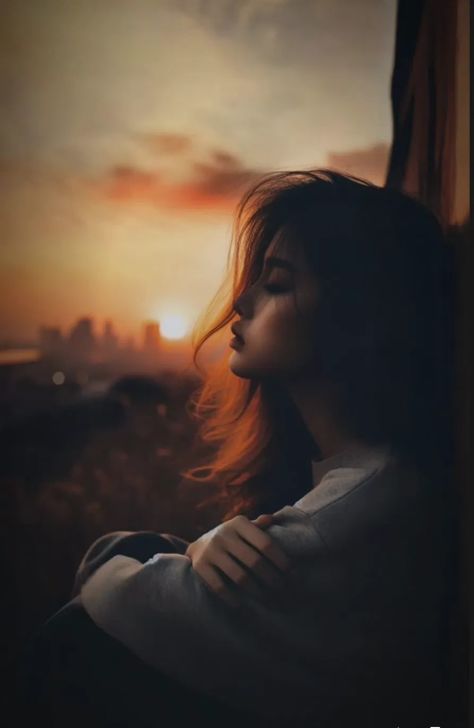 A photorealistic young woman with closed eyes sits curled beside a large window at sunset, wearing a heather-grey sweatshirt as copper-orange rim light outlines her wavy hair against a blurred city skyline.
